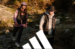 Two people walking along a rocky trail outdoors, wearing outdoor clothing and hats.