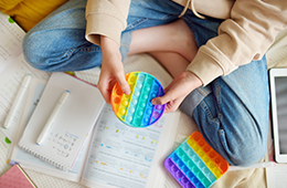 Student with a rainbow-colored interactive toy sitting on the ground with school notes