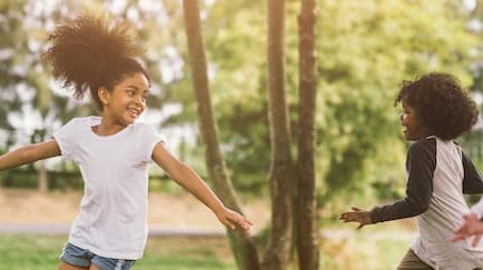 2 kids outdoors - one mid jump and the other mid run, with trees in the background