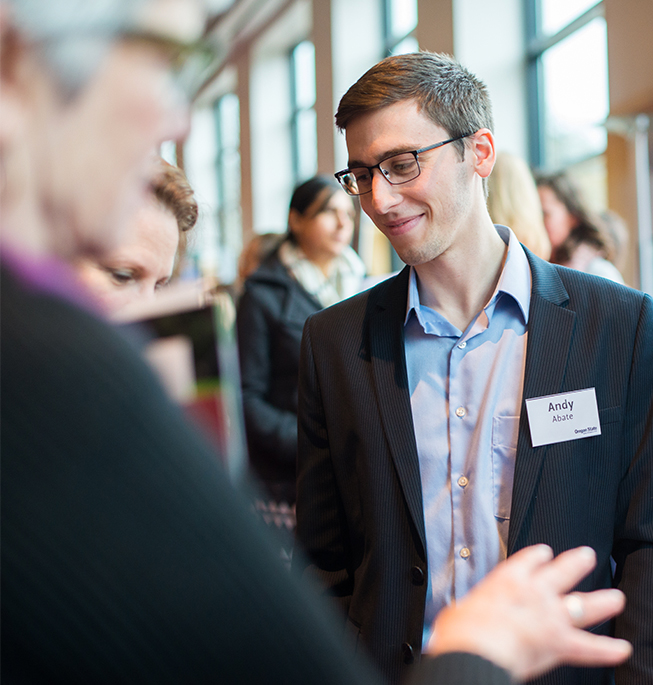 senior at OSU with a name tag and wearing proffesional clothing, he is smiling while interacting with OSU Alumni