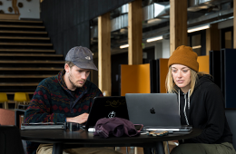 Two students using laptops seated at the same table in an OSU building