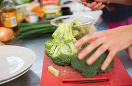 hand holding broccoli on a cutting board to prepare it for cooking