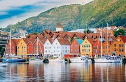Bergen's colorful coastal buildings by the water with sailboats and mountains in the background