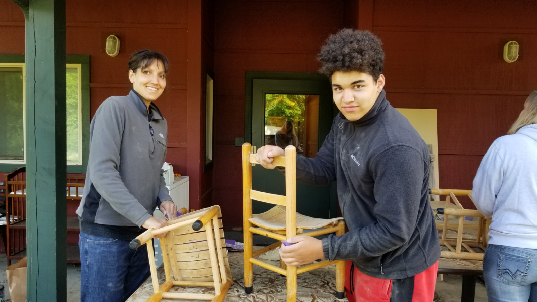 Two Day of Service Volunteers sanding child size wooden chairs.