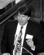 James Bernau speaking into a microphone, in black and white