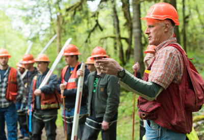 Kevin Lyons in a forest outside with a group of students, all wearing protective gear