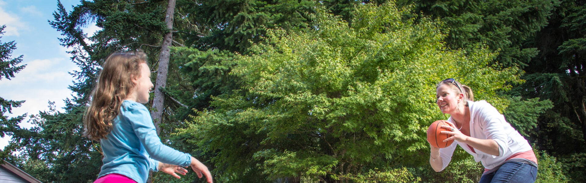 mother and daughter throwing a children's basketball back and forth outside