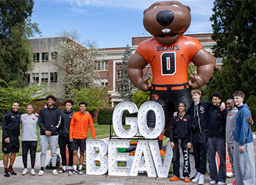 DPD_BigBenny_GroupPhoto_ImpactReport_2024 Group of students smiling in front of Big Benny and 'Go Beavs' marquee letters.