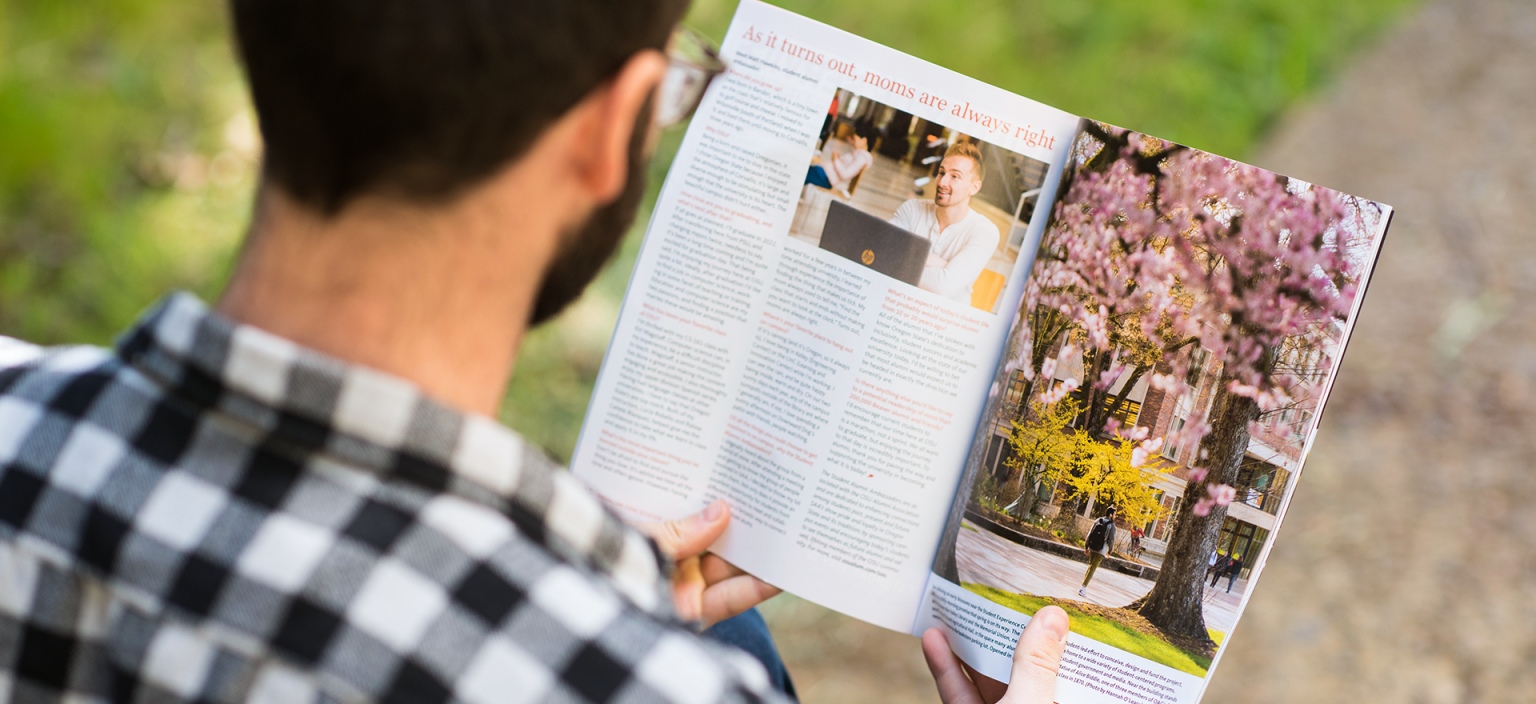 Looking over someone's shoulder as they read through an Oregon Stater magazine outside.