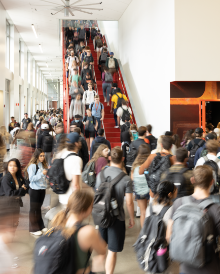 A crowded hall and stairway filled with students wearing backpacks.