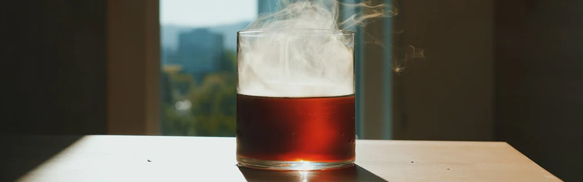 Cold old fashioned drink of a dark amber liquid with smoke.