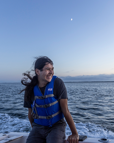Gabriel Jurado sitting on a boat, smiling and looking at the open sea at sunset.