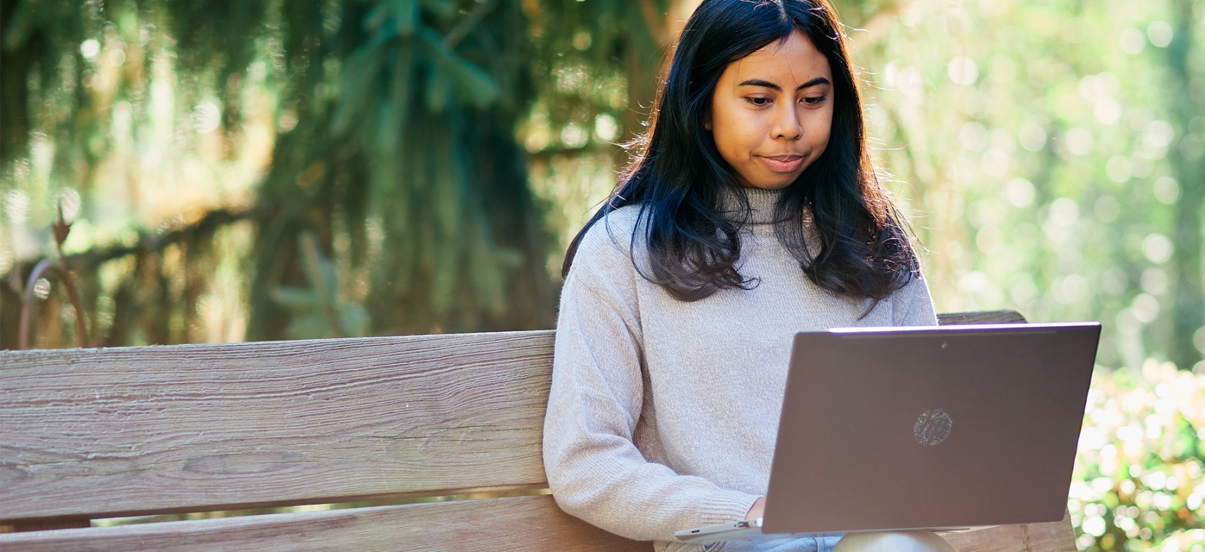 Afifah, student, sitting on a park bench using her laptop