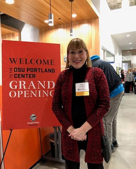 Professor of Art Emerita Kay Campbell at the OSU Portland Center next to sign that reads "Welcome to the OSU Portland Center Grand Opening""