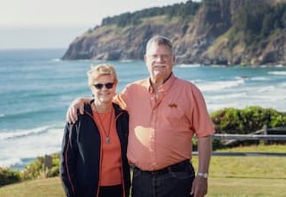 Nancy and Kent Searles outside, backgorund is the beautiful Oregon Coast on a clear day, ocean in the background