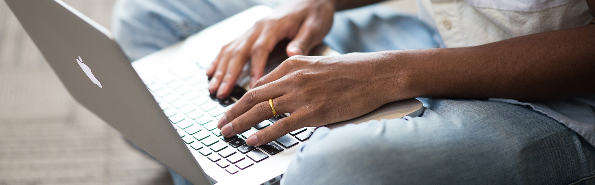 A macro view of someone's hands working on a laptop and sitting cross-legged on the floor.