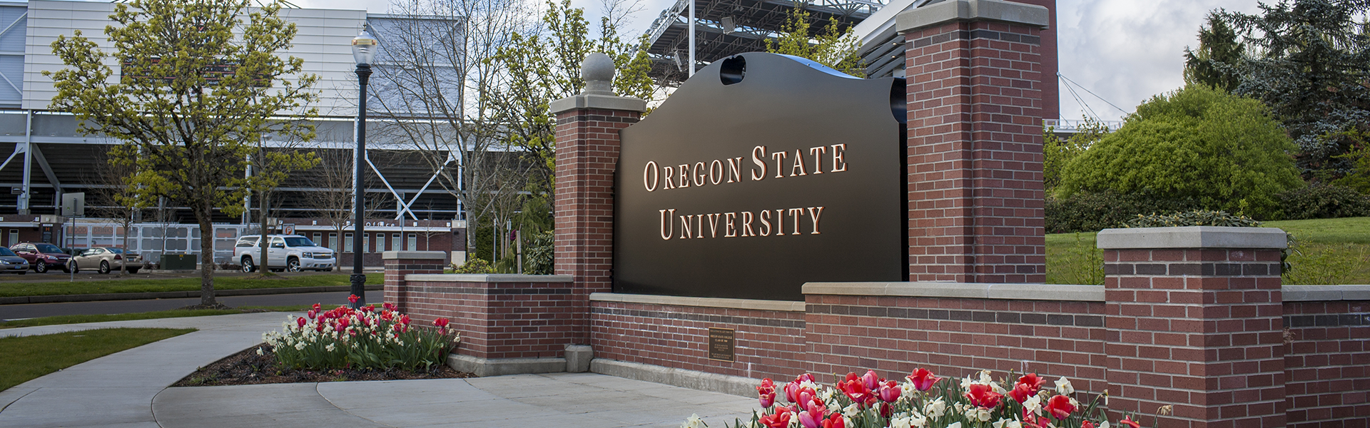 The Oregon State University sign surrounded by a brick structure with flower beds below