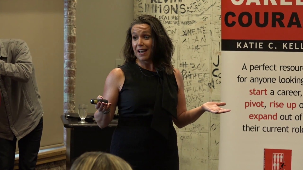 Katie Kelly speaking next to signage at an event