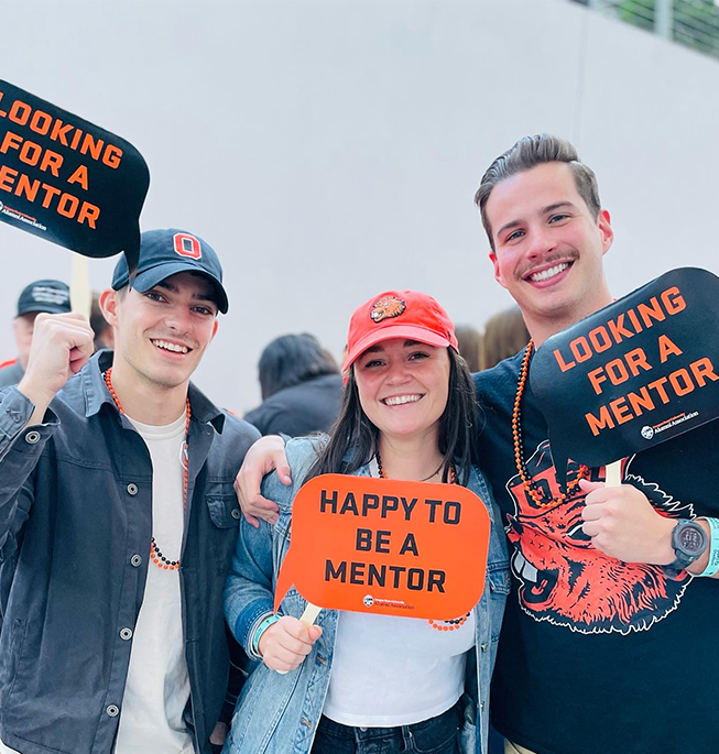 Three smiling young people holding signs about mentorship