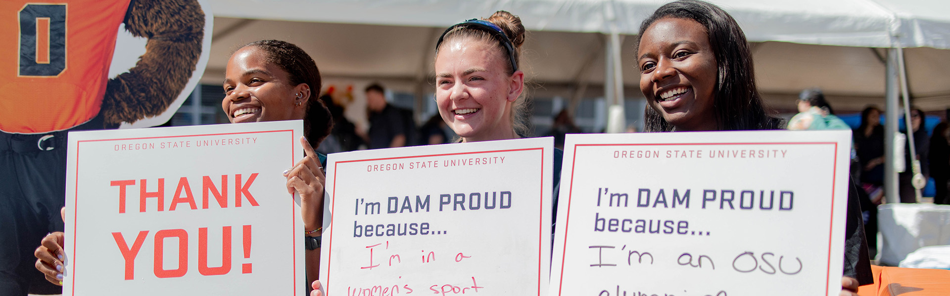 Three students holding signs that say "Thank You" and "I'm Dam Proud because..."
