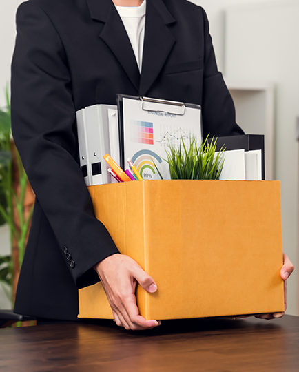 Person in a blazer holding a cardboard box with office items.