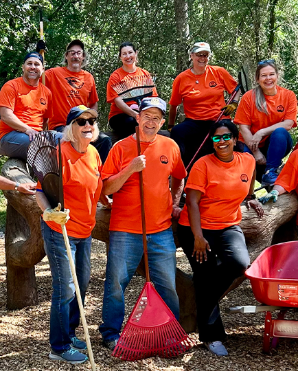 OSU volunteers in orange shirts hold wheelbarrows, rakes and other garden tools.