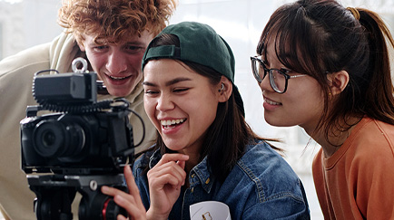 Three people looking at the display on a camera.