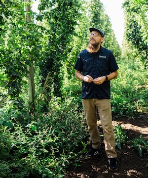Virtual Tasting Speakers_OSUAA-02 Person standing in a hop field surrounded by tall hop vines and greenery.