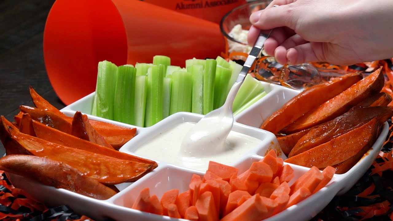 A tray with buffalo potato wedges, celery, carrots, and a ranch dip in the middle