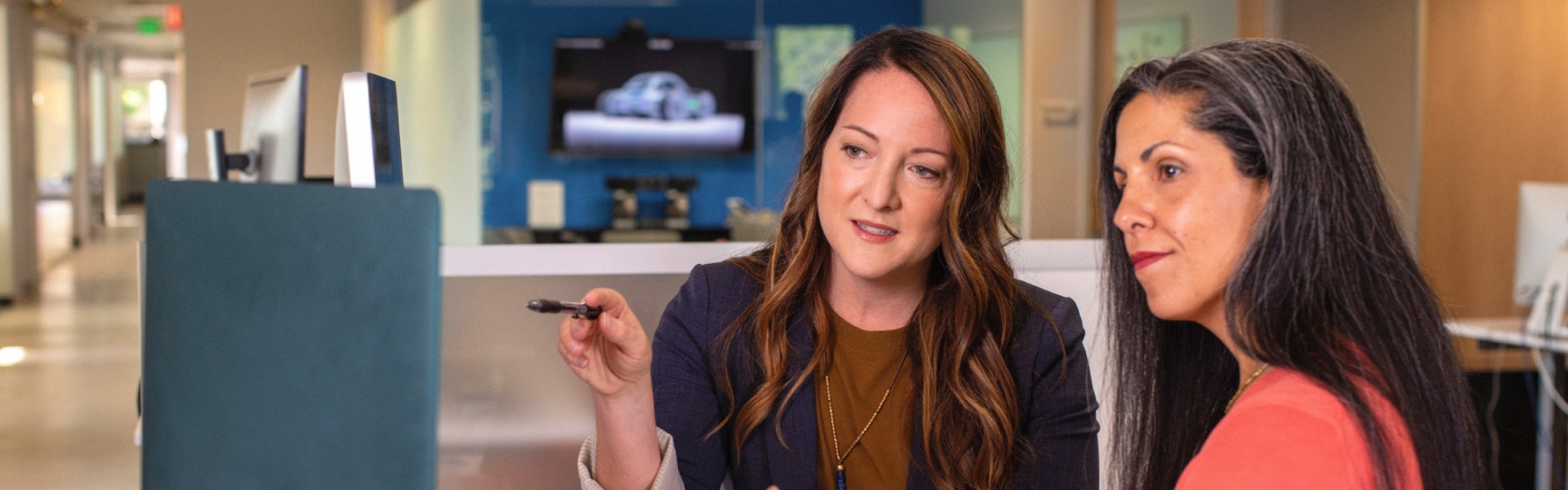 Two female coworkers discussing something that is on a computer.