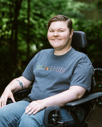 Kolbey Bonin in his wheelchair surrounded by beautiful greenery and dappled light.
