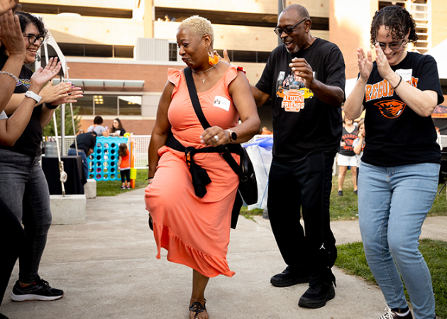 A woman in an orange dress dancing in front of a smiling, clapping crowd.
