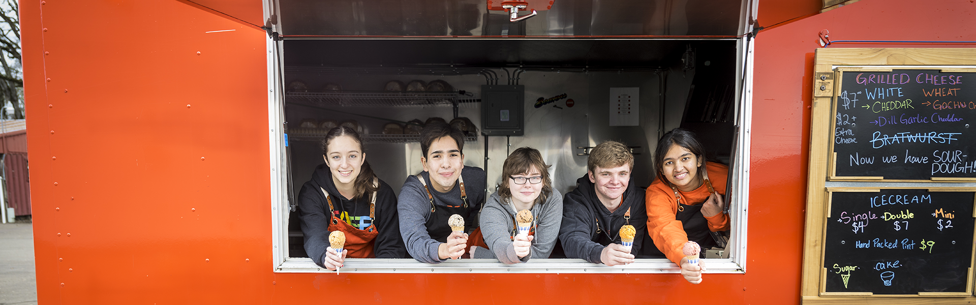 students leaning out of food truck window with ice cream cones in outstretched hands