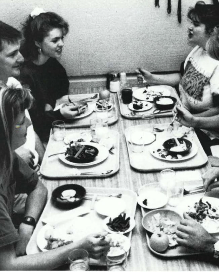 Black and white photo taken in 1992 of students with lunch trays eating at a lunch table